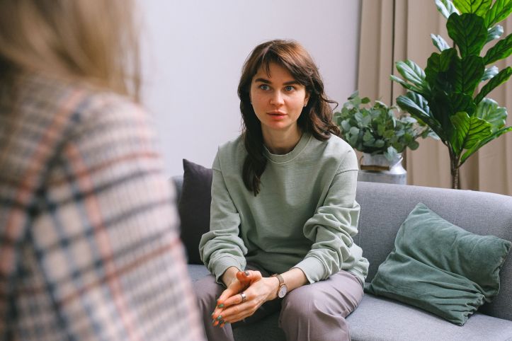 Jonge vrouw zit op bank in gesprek met andere vrouw