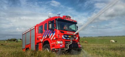 Foto van een natuurbrandvoertuig in een weiland met een werkende waterspuit aan de voorzijde.