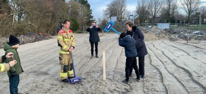 brandweerman en burgemeester staan bij de eerste paal van de nieuwe kazerne. Kind met grote hamer slaat de paal.