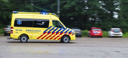Foto van een ambulance die langs een rij geparkeerde auto's rijdt 