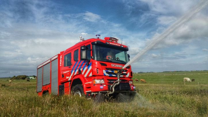 Foto van een natuurbrandvoertuig in een weiland met een werkende waterspuit aan de voorzijde.