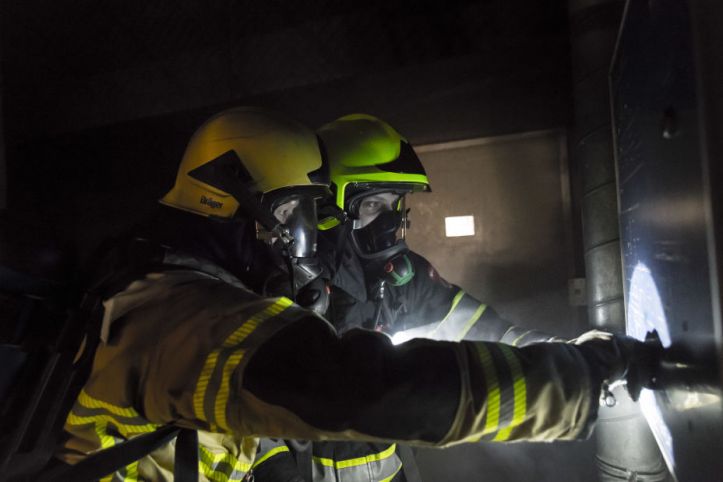 Foto van twee brandweermensen in opleiding die een oefening doen in een donkere ruimte.